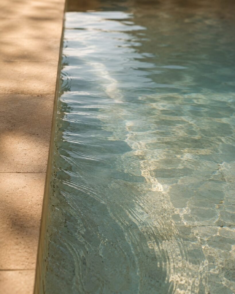 Clear pool water at a pale stone coping edge, fine ripples catching morning light, the result of good circulation rather than extra chemicals